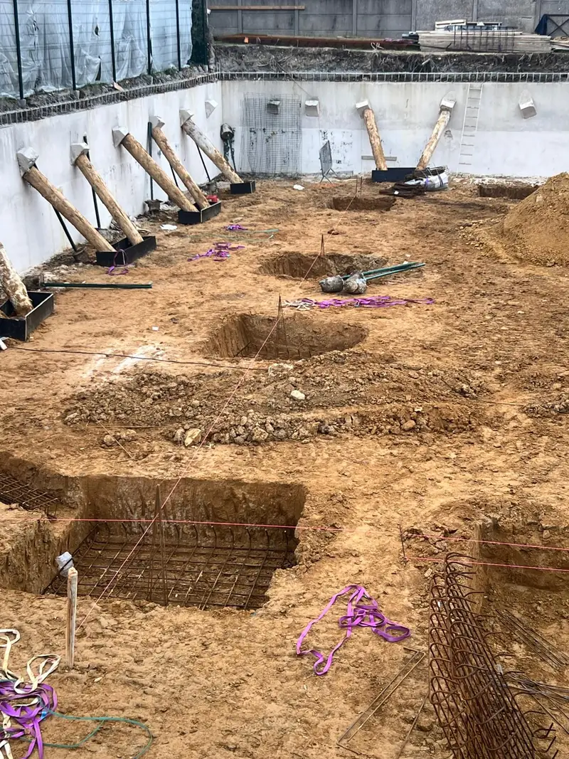 Paroi de fouille blanche maintenue par une rangée de rondins inclinés, fond de fouille en terre.