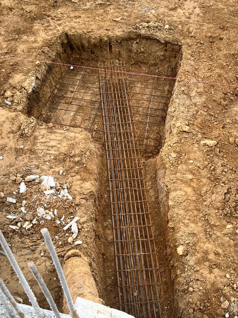 Tranchée de fondation avec armatures filantes reliées à une semelle carrée ferraillée.