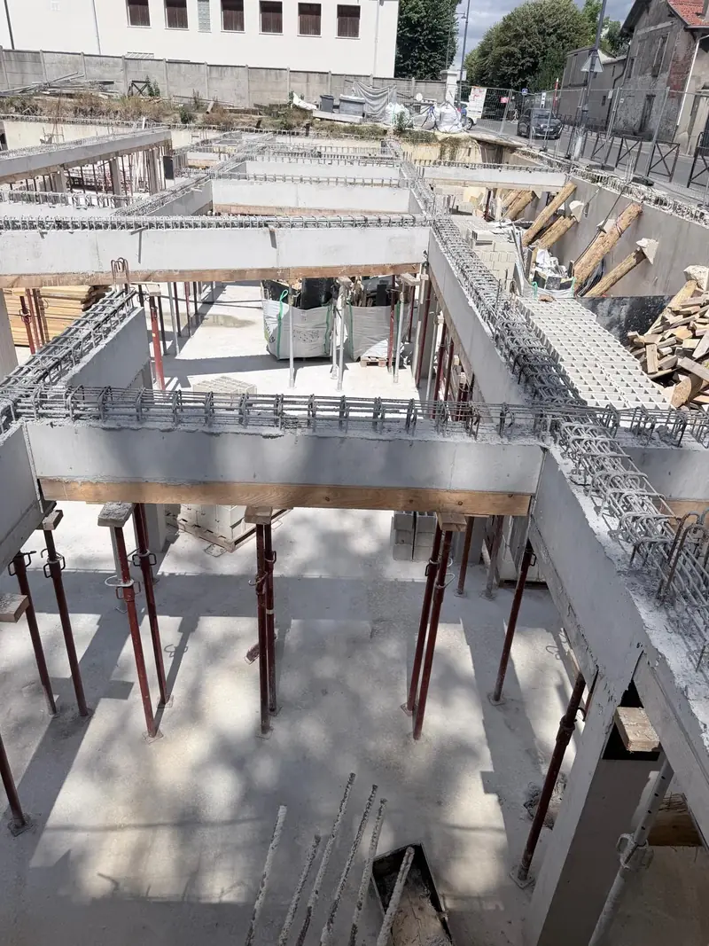 Poutres en béton coffrées en bois et étayées par des étais métalliques rouges au-dessus de murs en blocs.