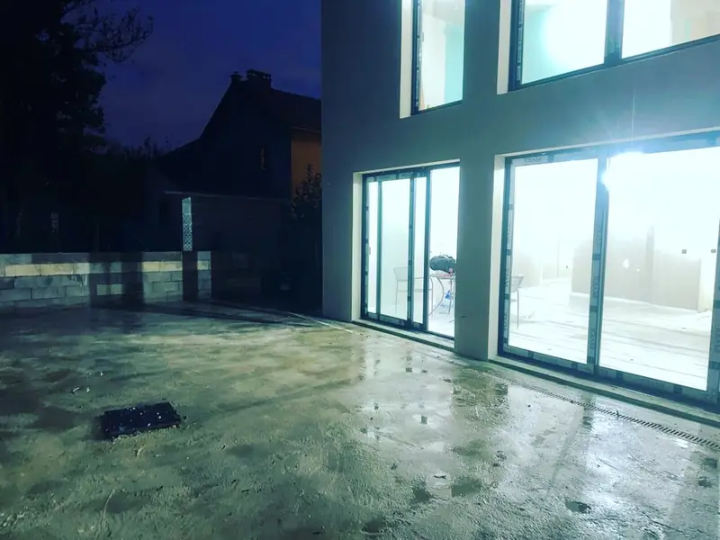 Terrasse en béton de nuit devant des baies vitrées éclairées.