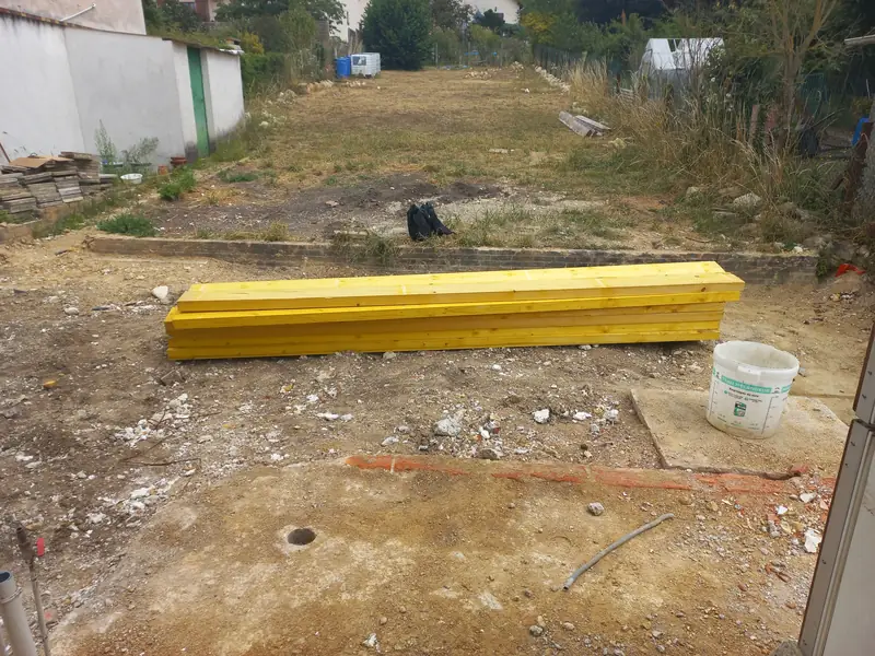 Jardin en longueur, terre à nu, madriers au premier plan.