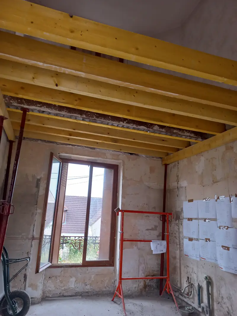 Plafond de solives bois neuves au-dessus d’une pièce en pierre, étais rouges.