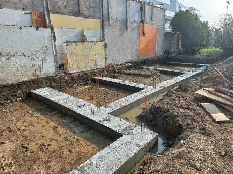 Semelles de fondation en béton coulées en forme de L, fers d’attente verticaux, fouilles humides autour.
