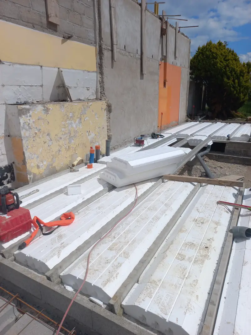 Plancher en cours de pose : entrevous blancs en polystyrène entre des poutrelles béton, sur un soubassement en blocs.