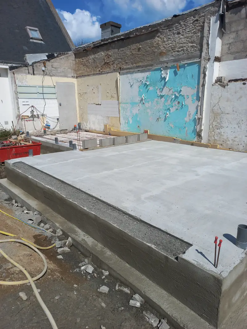 Dalle de béton lisse et fraîchement coulée sur son soubassement, tuyaux de réseaux en attente.