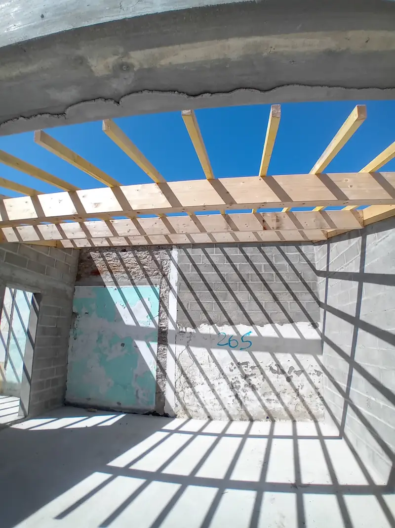 Vue vers le ciel à travers un solivage en bois clair posé sur des murs en blocs béton.