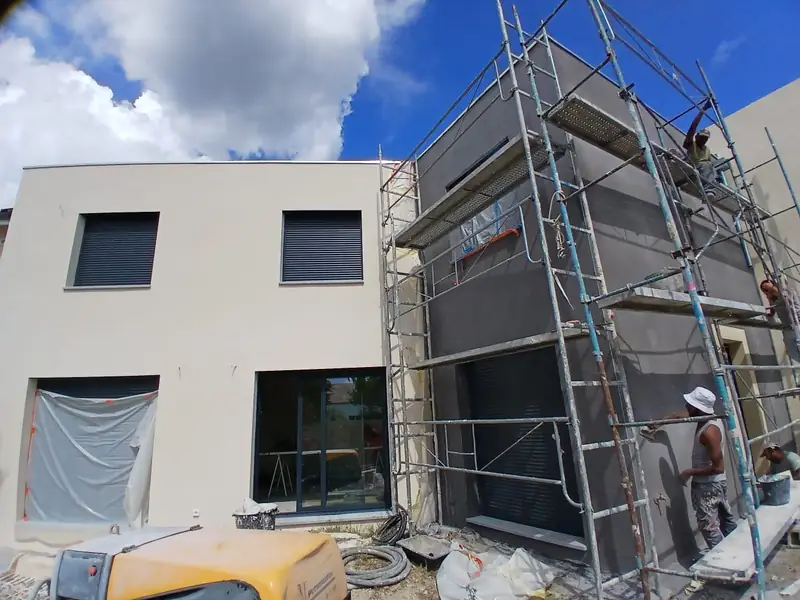 Façade arrière sous échafaudage, enduit clair d’un côté, enduit gris foncé en cours de l’autre.
