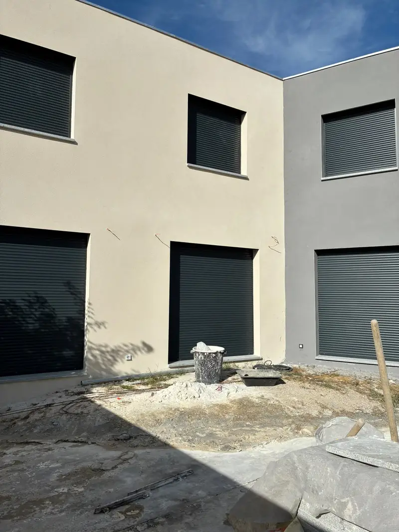 Angle de façades enduites claires avec fenêtres anthracite à volets roulants.