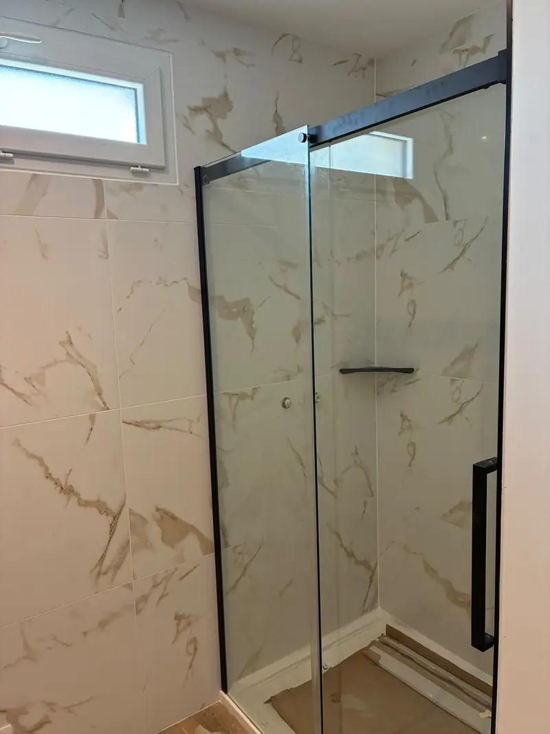 Douche avec paroi vitrée à profilés noirs, faïence blanche veinée de doré, petite fenêtre haute.