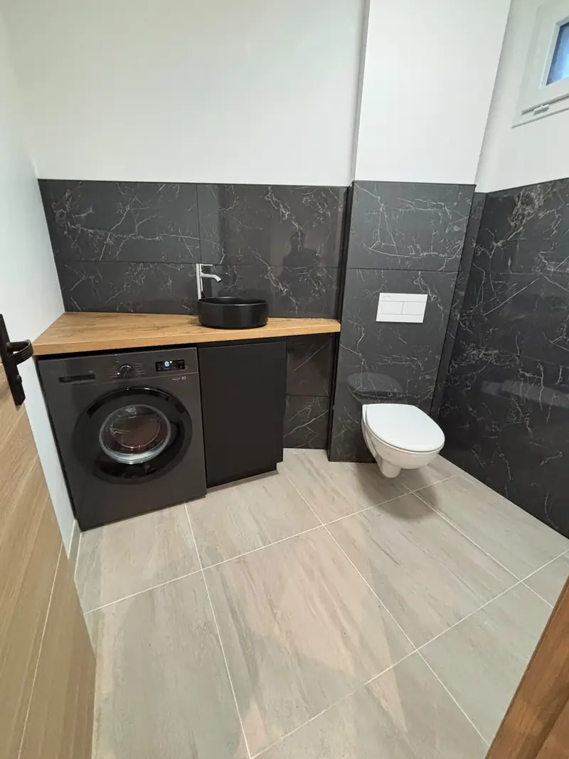 Pièce d’eau avec faïence effet marbre noir, plan vasque en bois, vasque noire et WC suspendu.