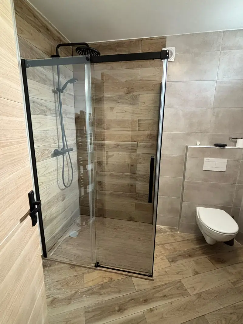 Douche à paroi noire et carrelage effet bois, WC suspendu.