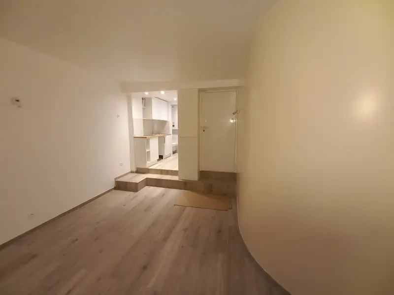 Couloir avec mur courbe blanc menant à l’estrade de la cuisine, spots au plafond.