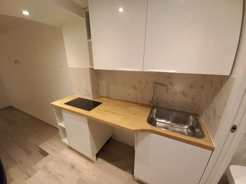 Cuisine blanche avec plan de travail en bois, évier inox, plaque de cuisson et crédence effet marbre.