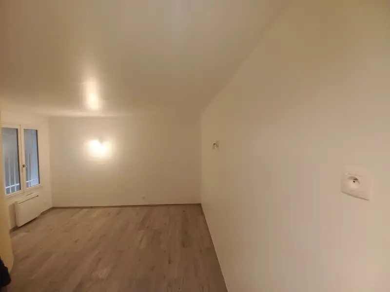 Pièce vide avec sol stratifié clair, appliques murales, fenêtre et radiateur.