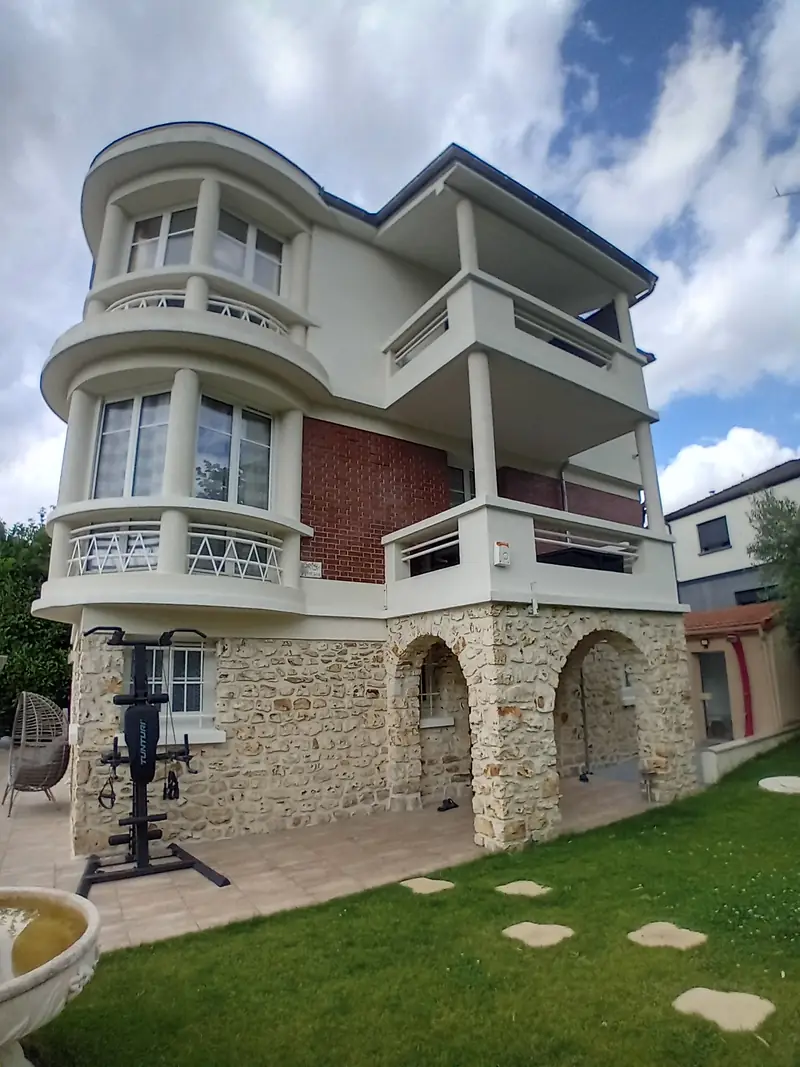 Villa de trois niveaux : soubassement en meulière à arcades, étage en brique rouge, niveau ajouté en enduit clair avec bow-window arrondi et loggia sur colonnes.
