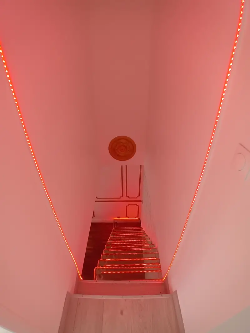 Escalier étroit vu d’en haut, murs éclairés par un ruban lumineux rouge.